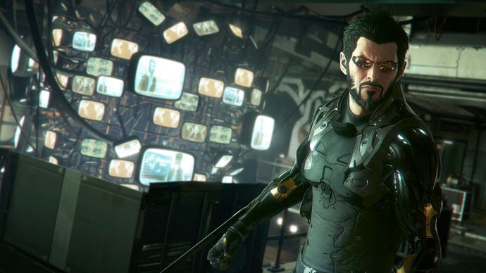 Adam Jensen stands facing away from a large wall filled with glowing TV screens.