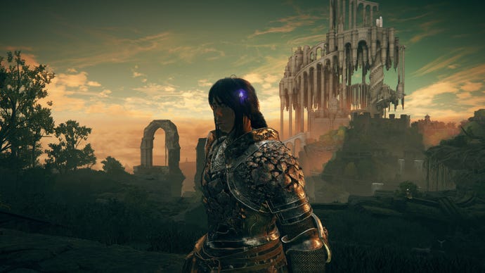 The player in Elden Ring: Shadow Of The Erdtree stands in Rauh Ancient Ruins with Enir-Ilim in the distant background. In the player's hair is St. Trina's Blossom, a purple flower.